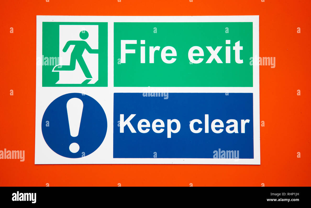 Safety signs indicating a fire exit and keep clear against an orange