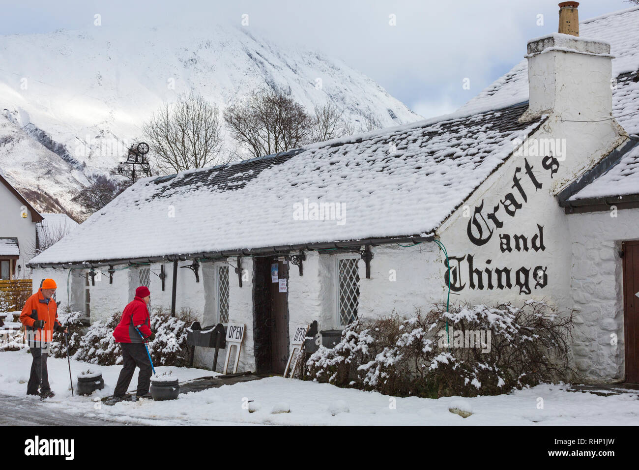 Walkers head for Crafts and Things shop and café covered in snow on a cold winters day at Glencoe Village, Highlands, Scotland in winter Stock Photo