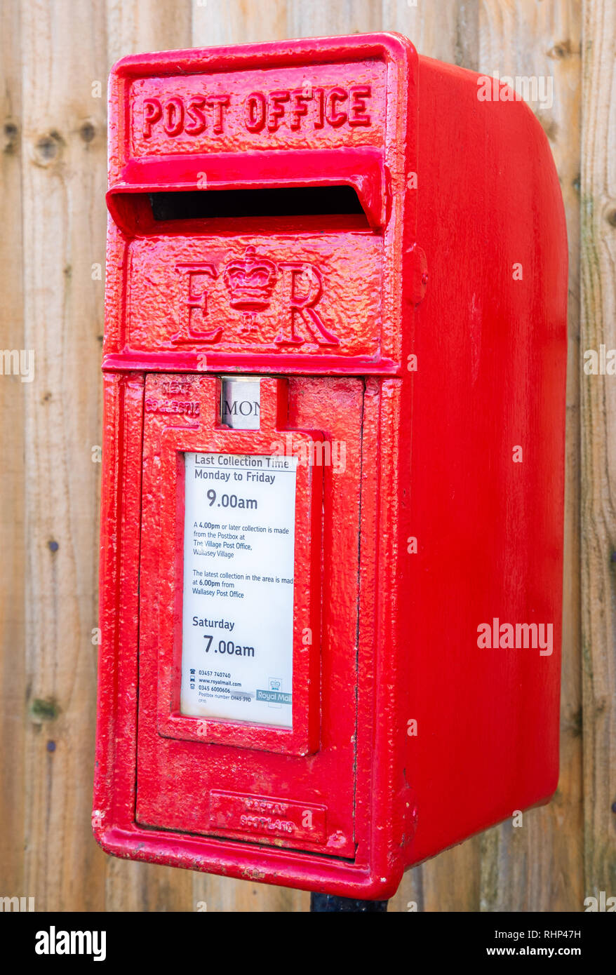 Close up of a red polemounted post box showing collection times by a wooden fence Wallasey Village February 2019 Stock Photo