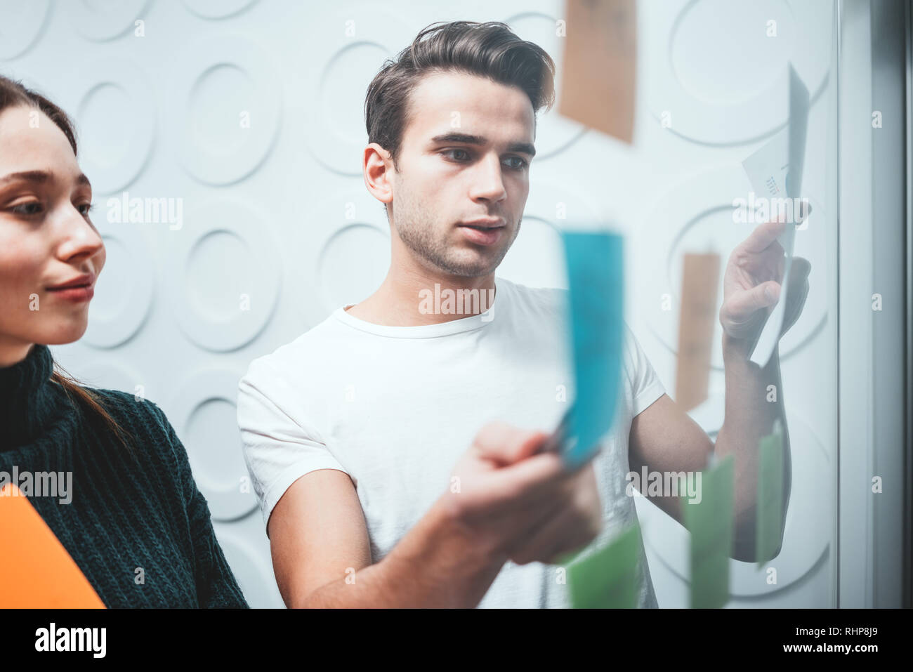 Portrait of two coworker people standing at office space behind glass wall with sticky notes. Team of manager disscusing and brainstorming new sturtup Stock Photo