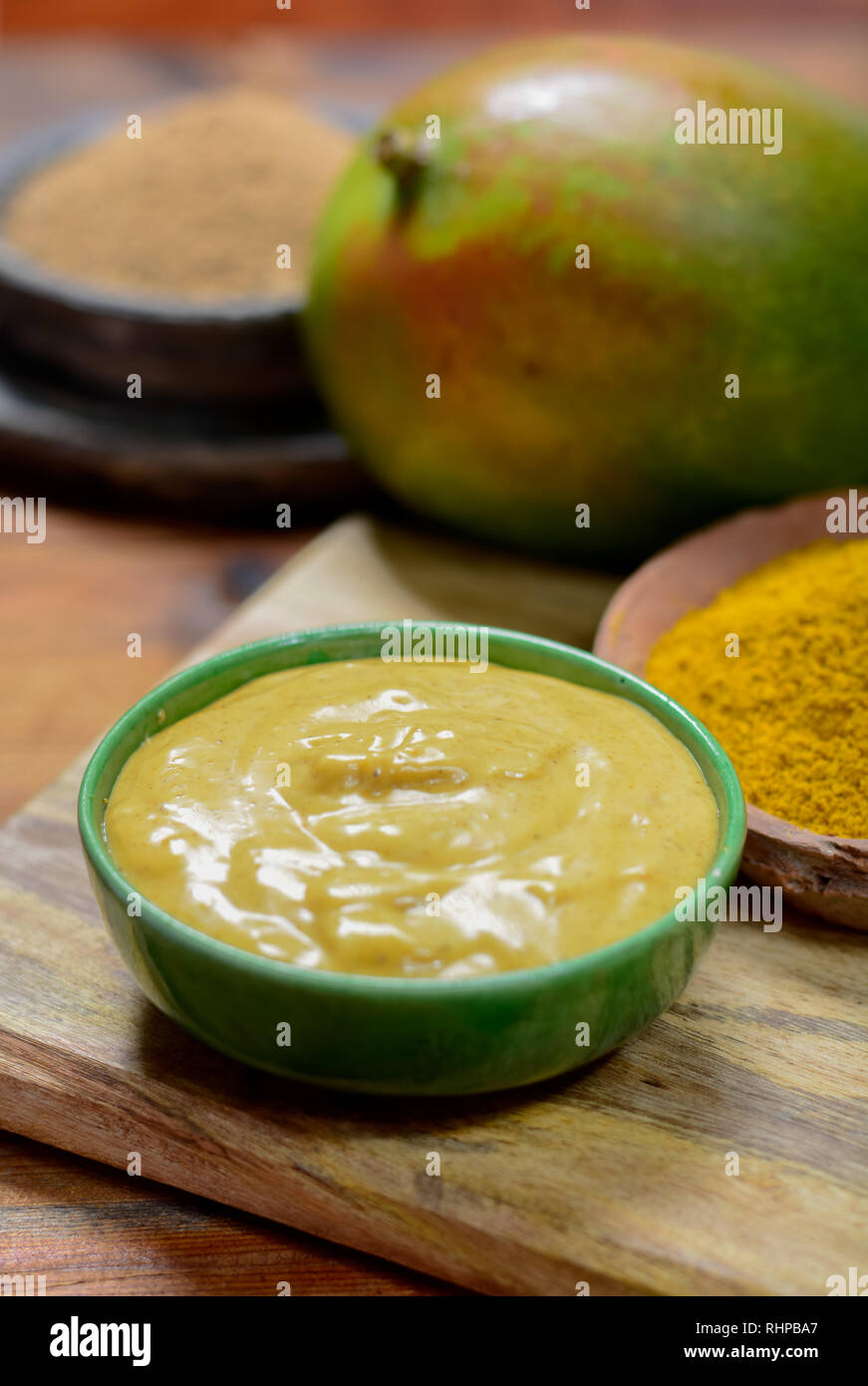 Tasty mango-curry sauce in small bowl ready to eat and bowls with mango and curry powder close- up Stock Photo