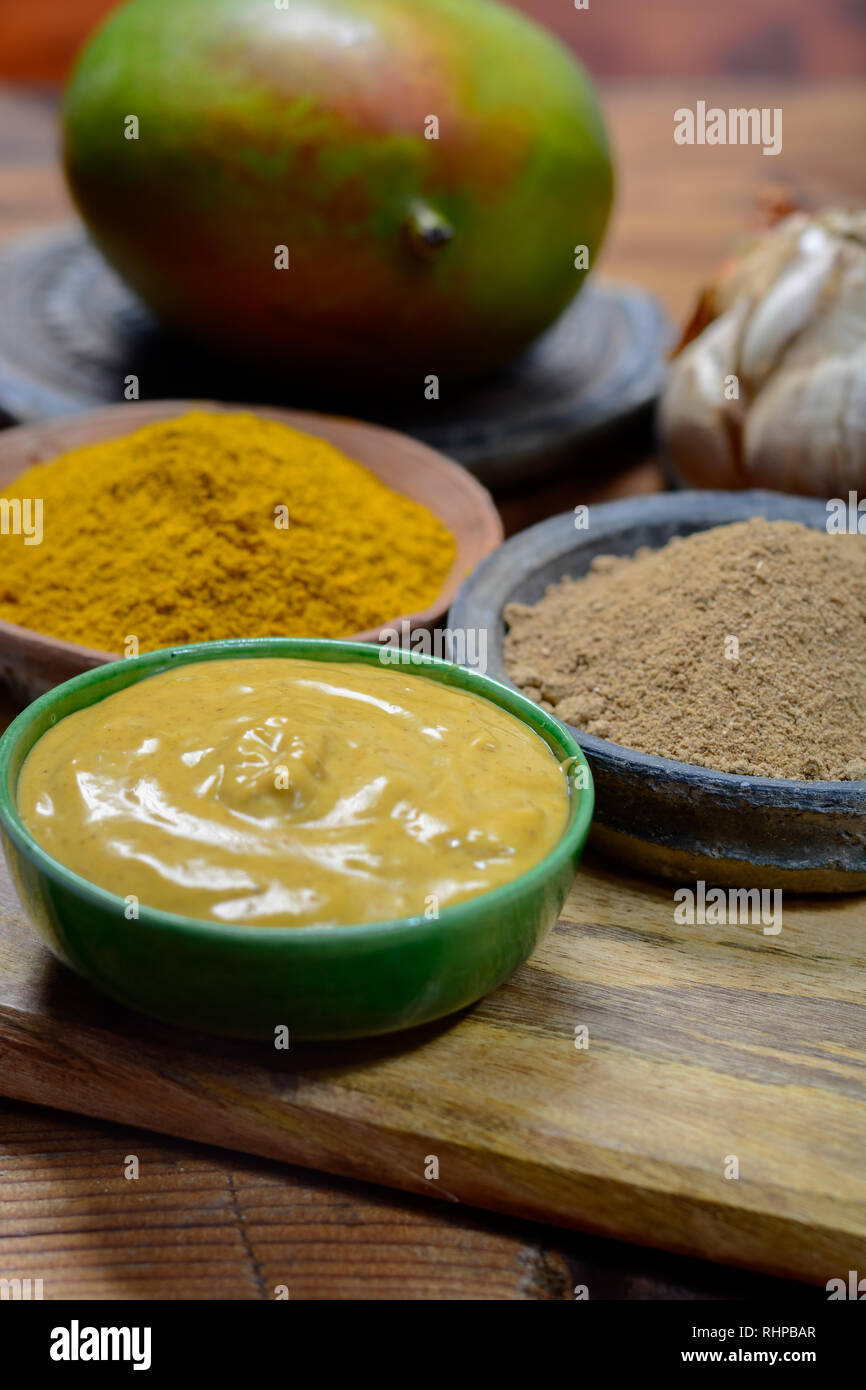 Tasty mango-curry sauce in small bowl ready to eat and bowls with mango and curry powder close- up Stock Photo