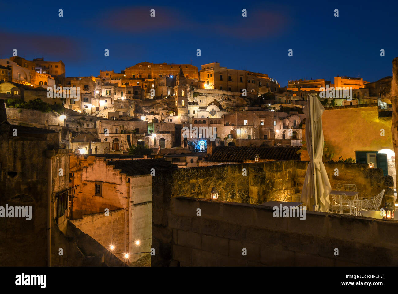 Evening view of the ancient city of Matera, Italy, with the colored lights highlighting patios of sidewalk cafes and churches in the historic village Stock Photo