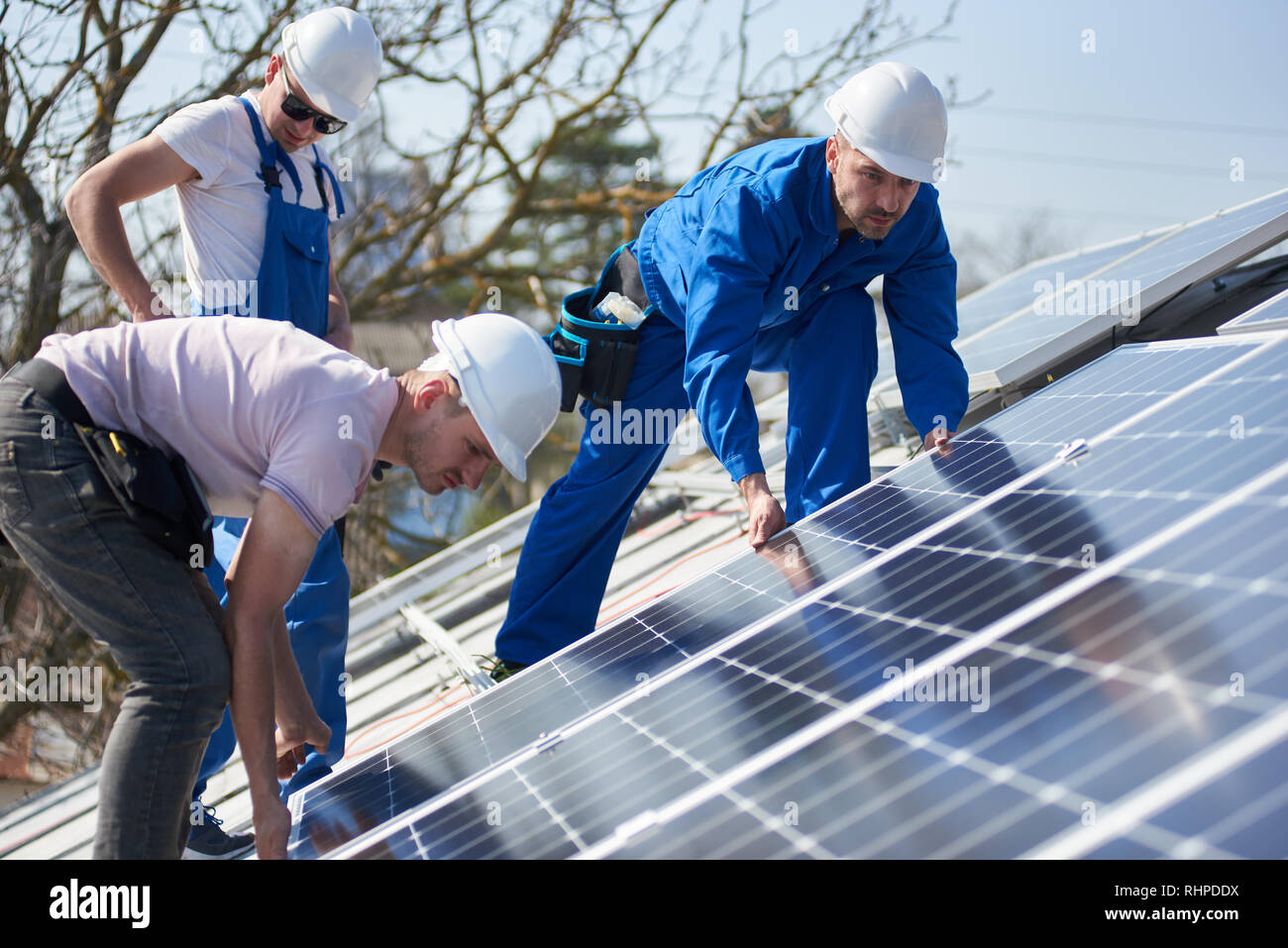 Male engineers installing stand-alone solar photovoltaic panel system. Electricians mounting blue solar module on roof of modern house. Alternative energy ecological concept. Stock Photo
