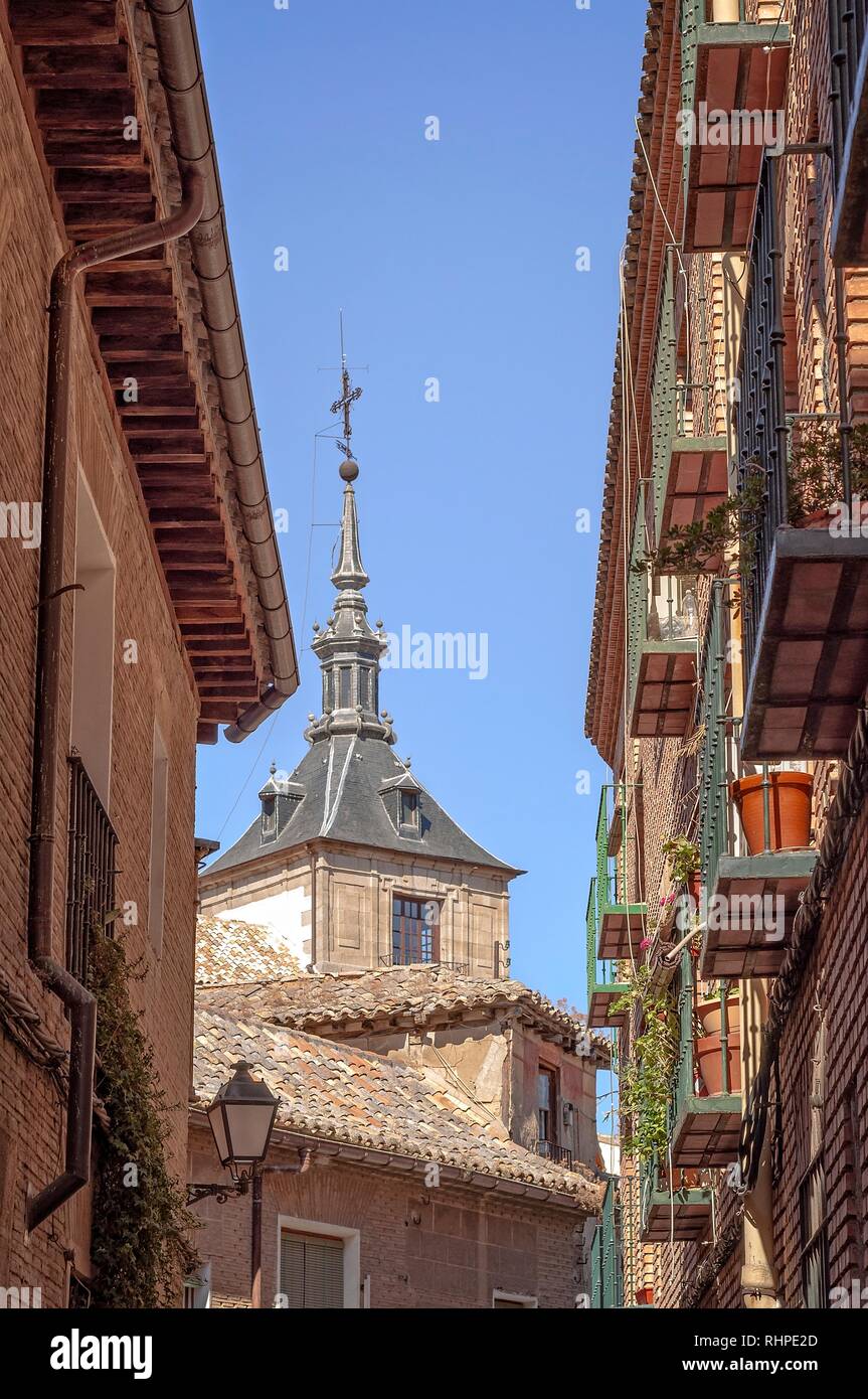 A typical street in Toledo with balconies on on side.  A church tower is in the background and a clear blue sky is above. Stock Photo