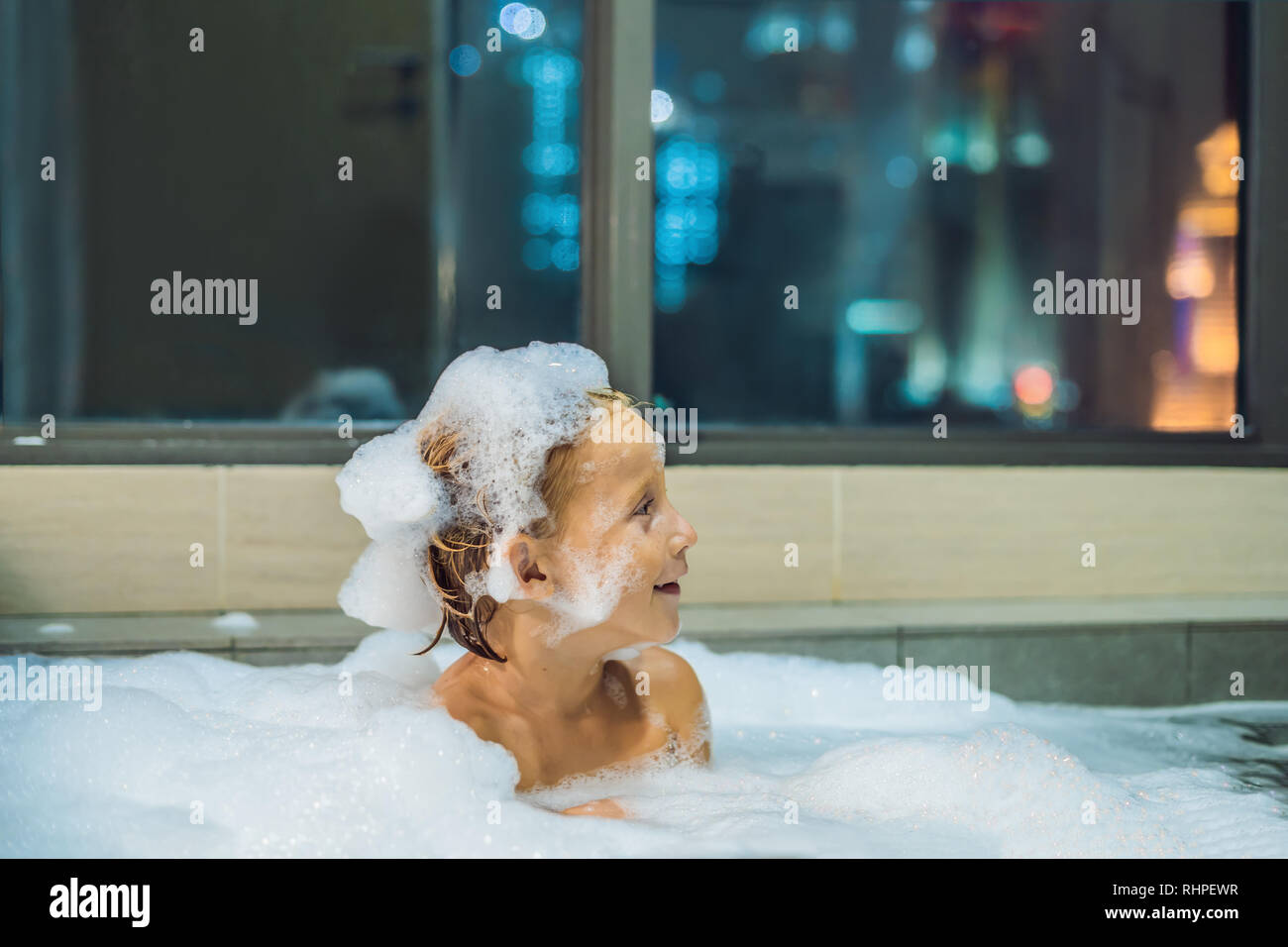 Happy little baby boy sitting in bath tub in the evening before going to sleep on the background