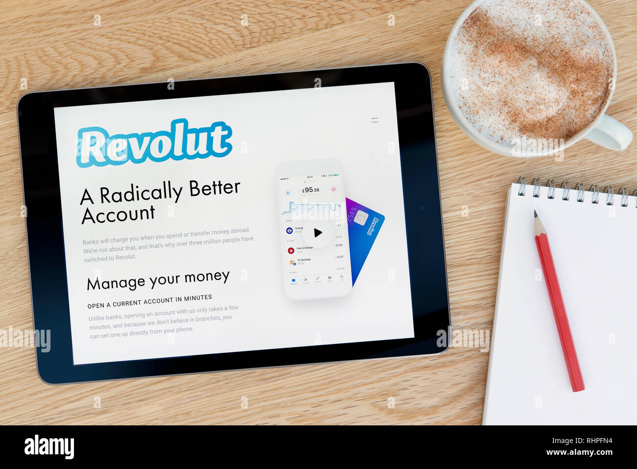 The Revolut website features on an iPad tablet device which rests on a wooden table beside a notepad (Editorial use only). Stock Photo
