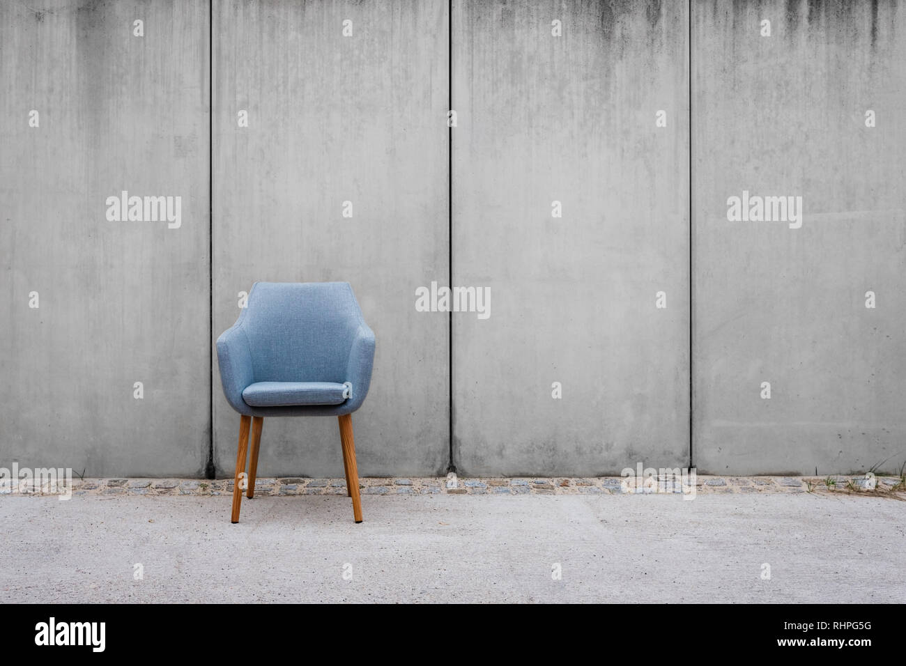 empty chair with concrete wall background on sidewalk - Stock Photo