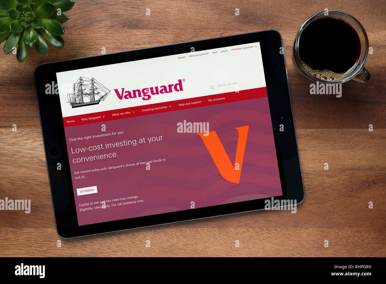 The website of Vanguard is seen on an iPad tablet, on a wooden table along with an espresso coffee and a house plant (Editorial use only). Stock Photo