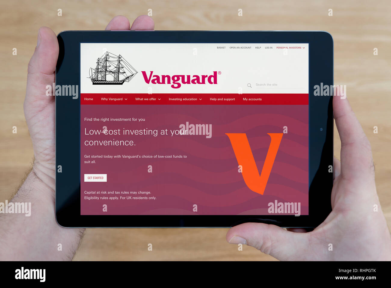 A man looks at the Vanguard website on his iPad tablet device, shot against a wooden table top background (Editorial use only). Stock Photo