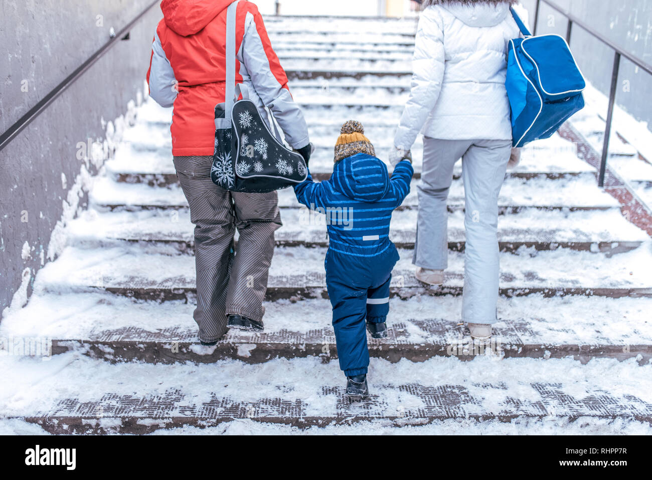 Mom and girlfriend sees the boy s son 4-7 years old by the hand walking down the street. Back view. Winter in city climb the stairs.. Returning home Stock Photo