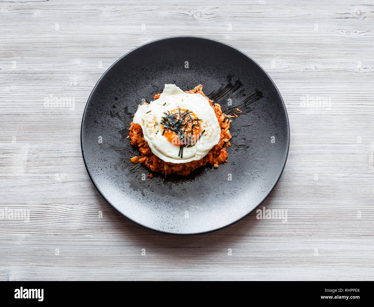 korean cuisine - top view of Kimchi bokkeum bap (fried rice with kimchi, beef and fried egg) on black plate on wooden board Stock Photo
