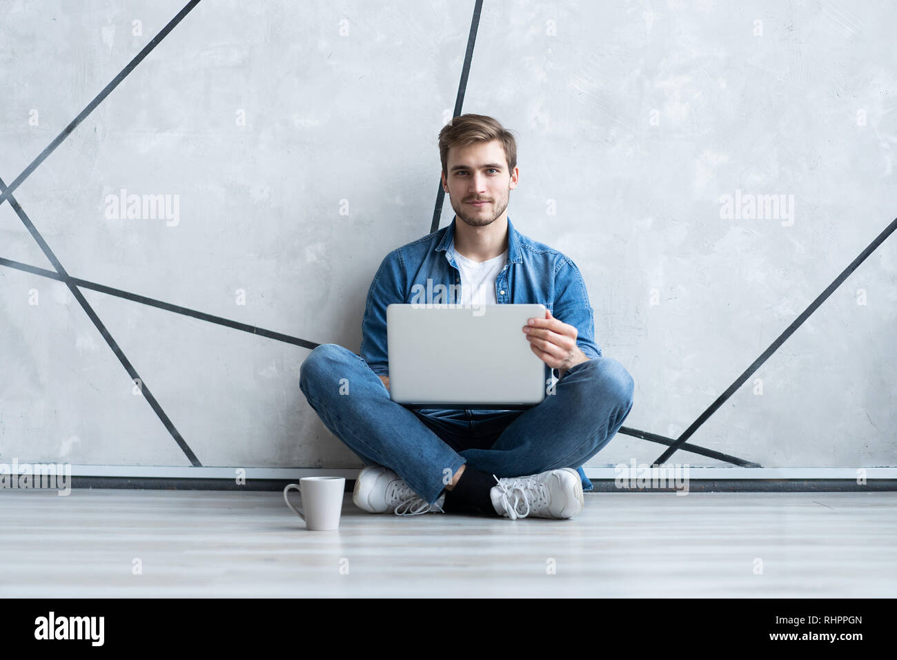 Young man working on laptop sitting on floor. Guy with computer reading ...