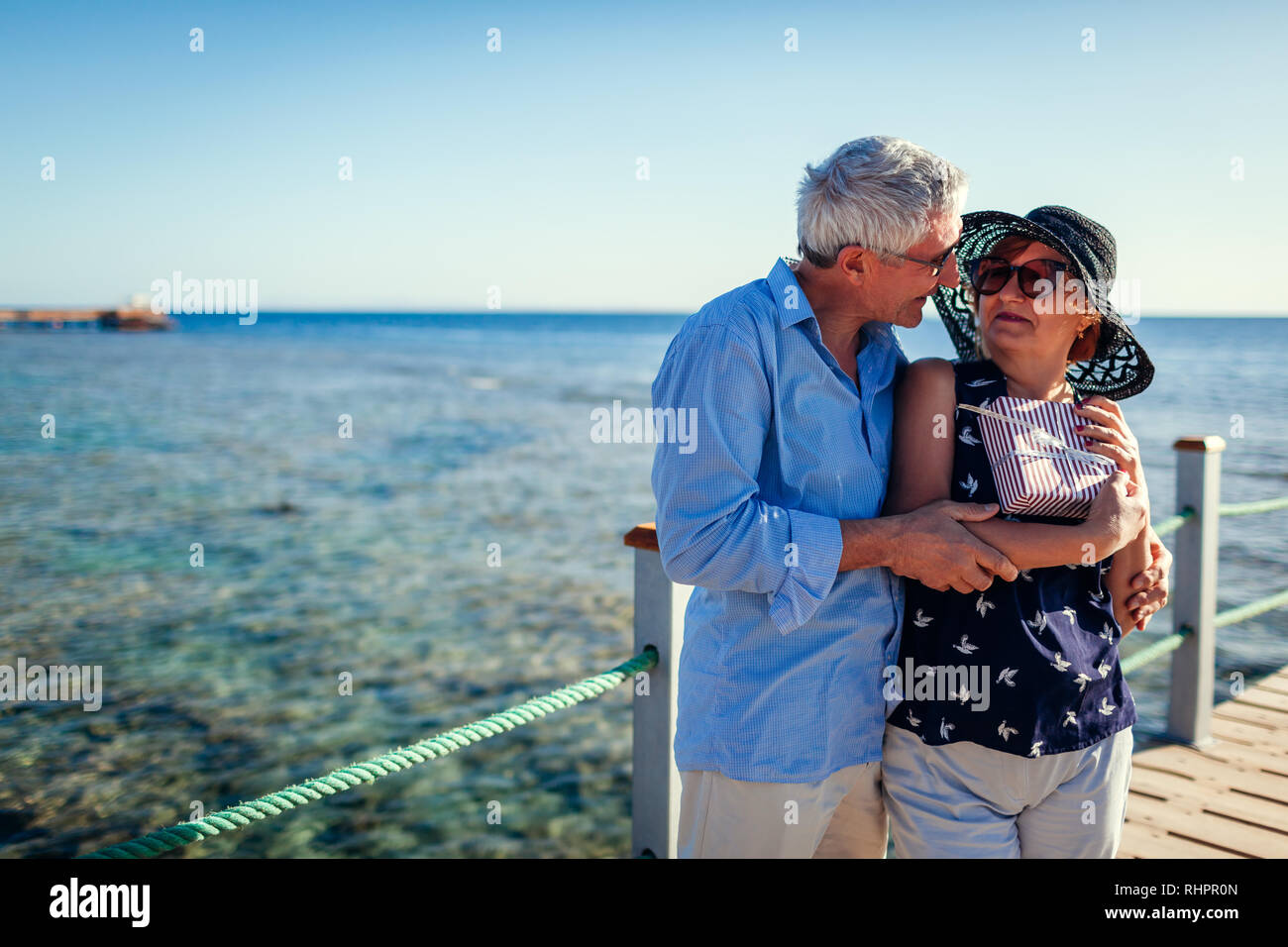 Senior couple walking on pier by sea presenting gifts for Valentine's day. People enjoying vacation. Stock Photo
