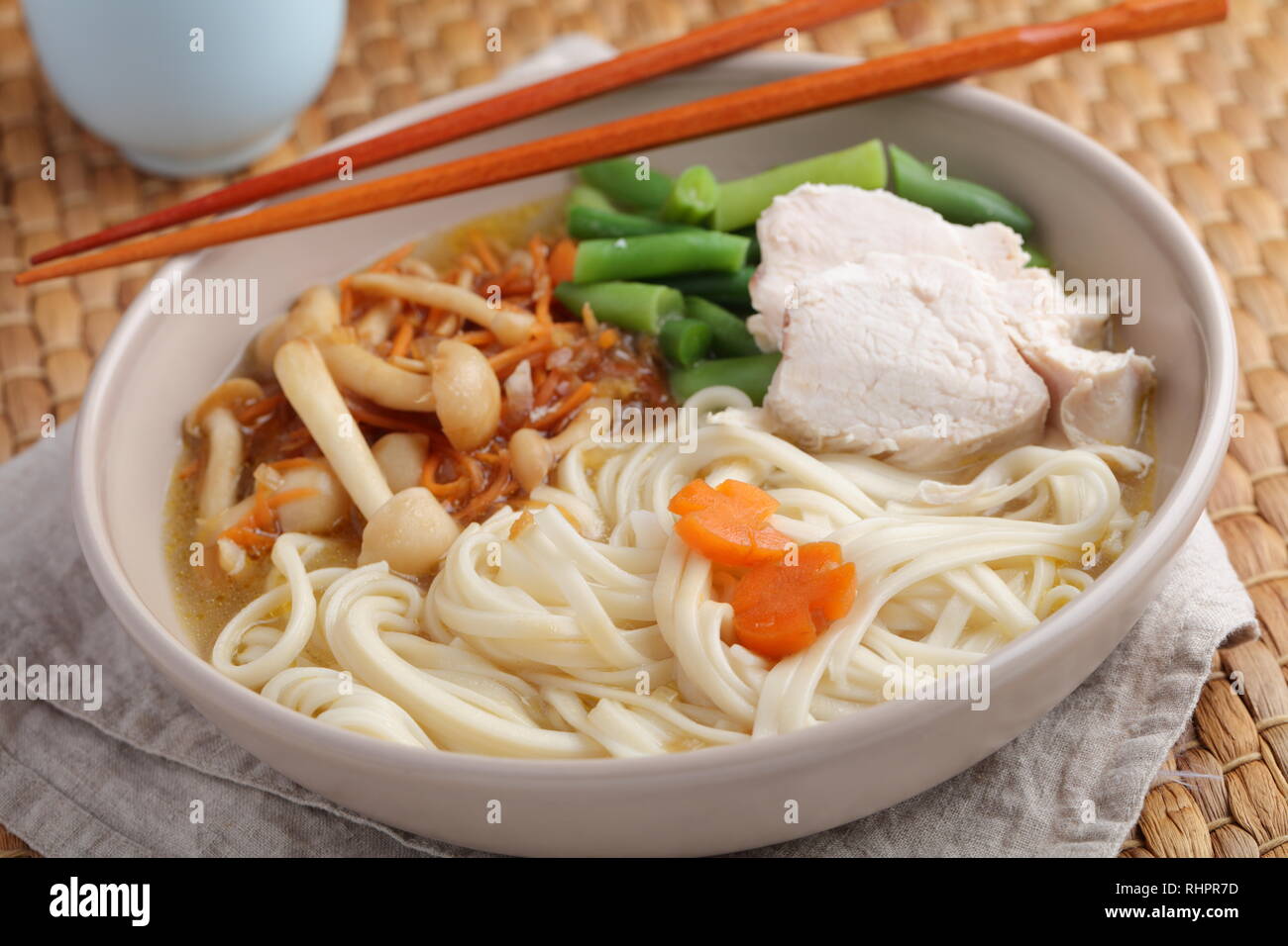 Chicken and udon noodle soup with Shimeji mushrooms, carrot, onion, and asparagus beans Stock Photo