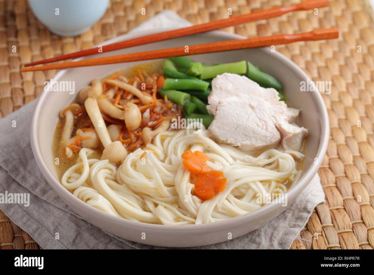 Chicken and udon noodle soup with Shimeji mushrooms, carrot, onion, and asparagus beans Stock Photo