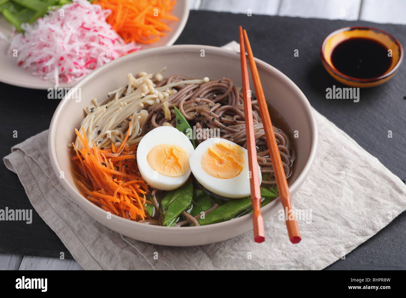 Japanese soup with Enoki mushrooms, soba noodles, boiled egg, carrot, radish, green beans, and soy sauce Stock Photo