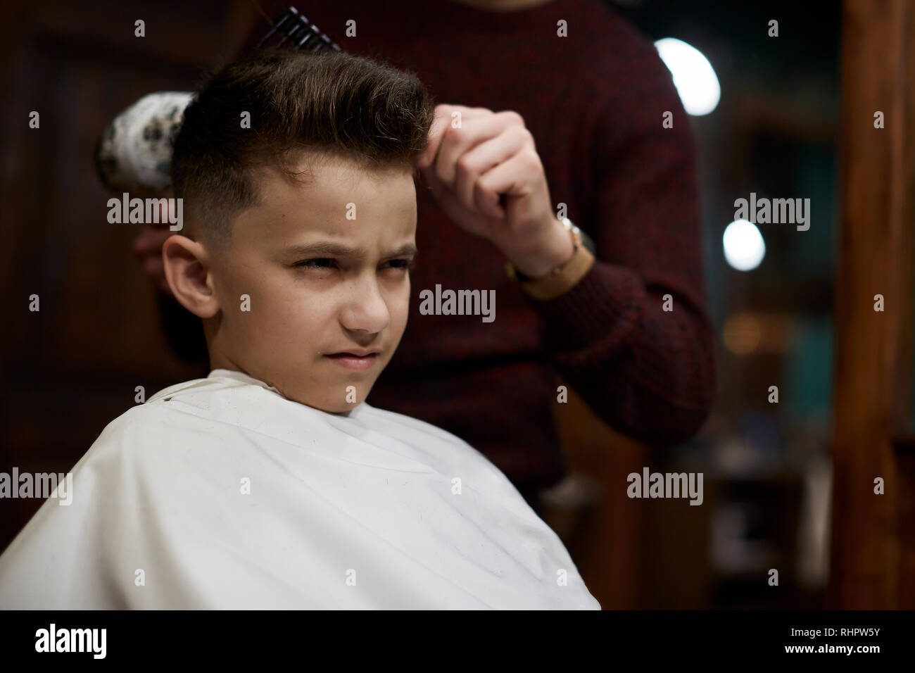 Children hairdresser cutting little boy against a dark background Stock Photo