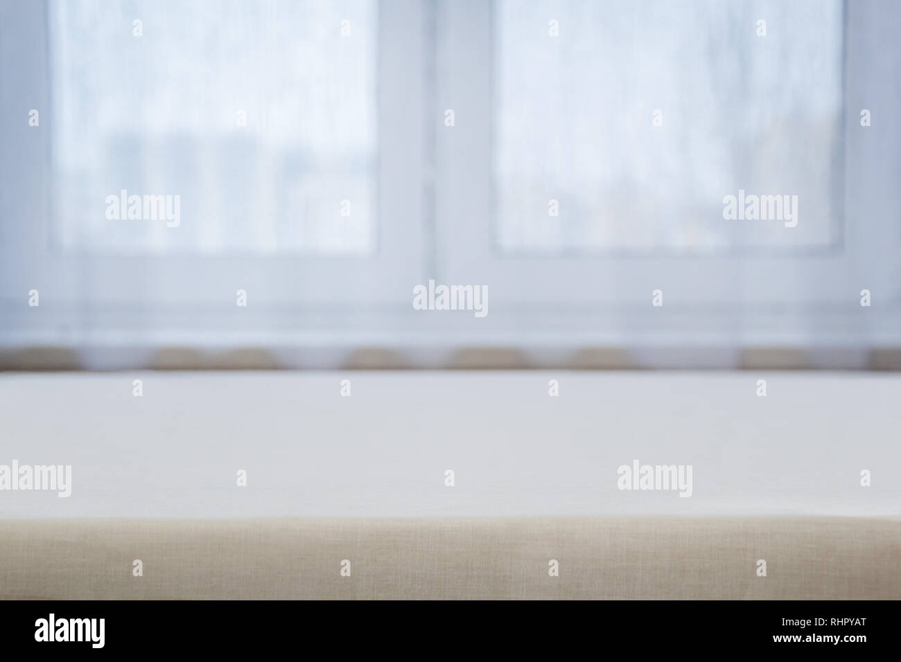 A table with a beige tablecloth against a white window Stock Photo