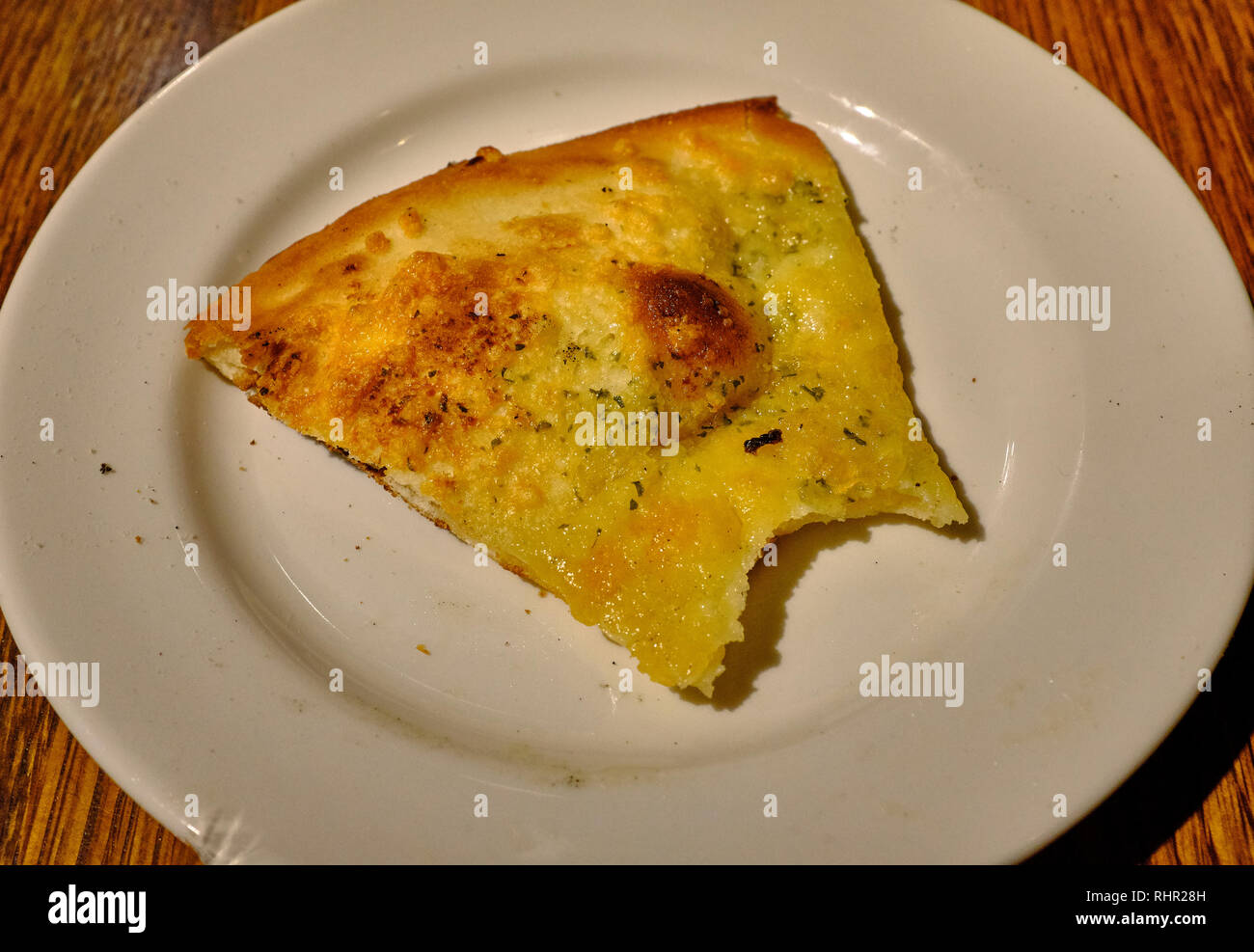 A single slice of stone baked flatbread with garlic butter that has partially been eaten on a white plate placed on a table Stock Photo