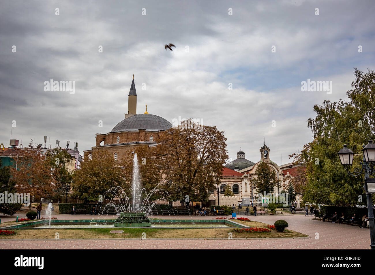 SOFIA, BULGARIA - OCTOBER 14, 2018: Many people enjoy sprinkling water of fountains in Banski Square in the Bulgarian capital. Moody cloudy sky autumn day. View from the staircase of History Museum Stock Photo