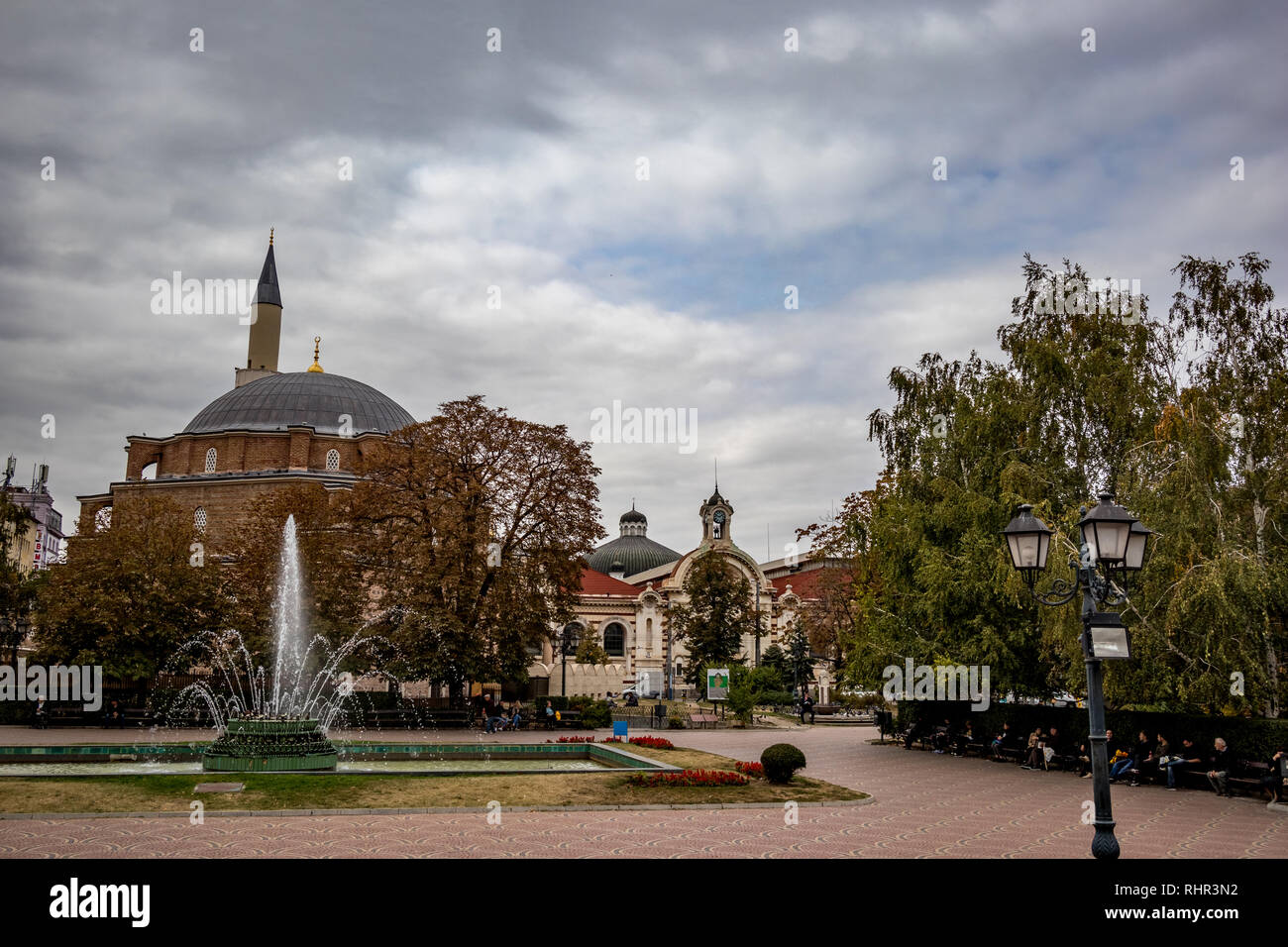 SOFIA, BULGARIA - OCTOBER 14, 2018: Many people enjoy sprinkling water of fountains in Banski Square in the Bulgarian capital. Moody cloudy sky autumn day. View from the staircase of History Museum Stock Photo