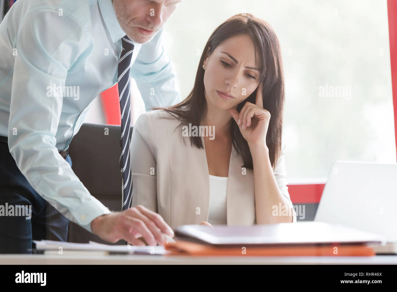 Businesswoman concentrating while colleague explaining at desk Stock Photo