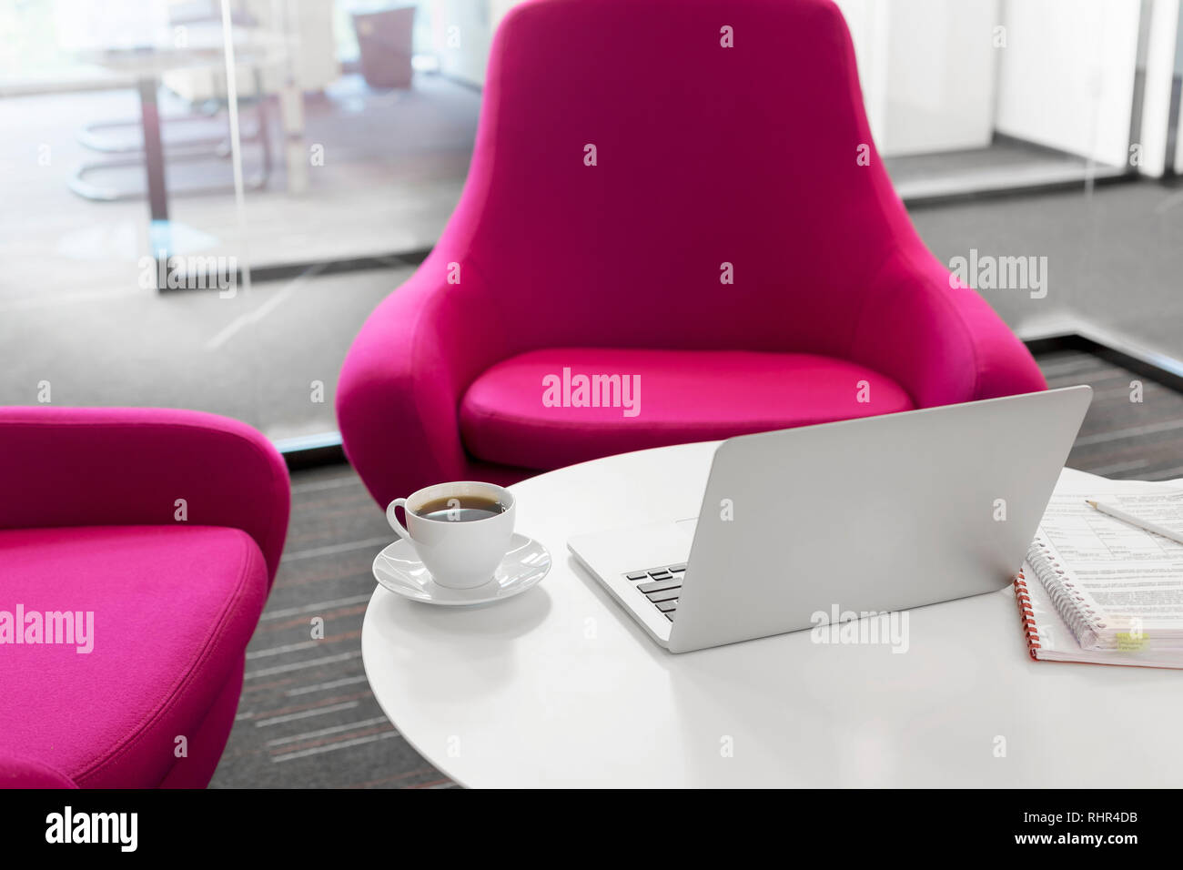 Laptop with coffee cup and file on table by pink chairs at office Stock Photo