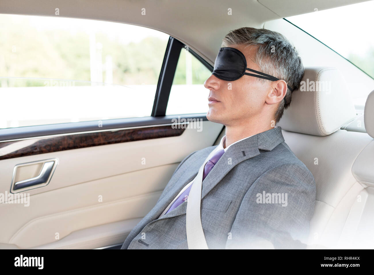 Mature businessman napping while wearing eye mask in car Stock Photo