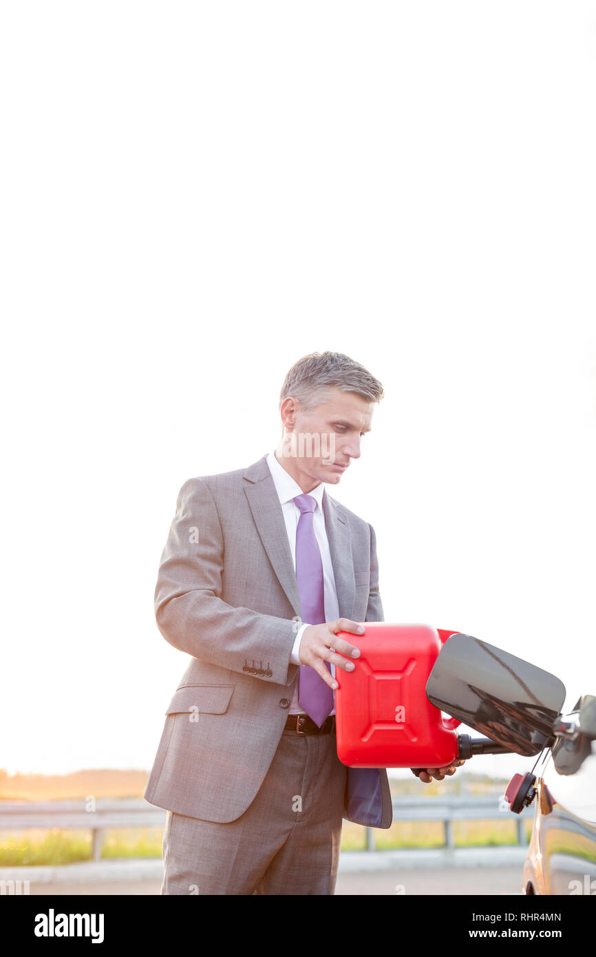 Businessman in formal fueling car with canister against sky Stock Photo