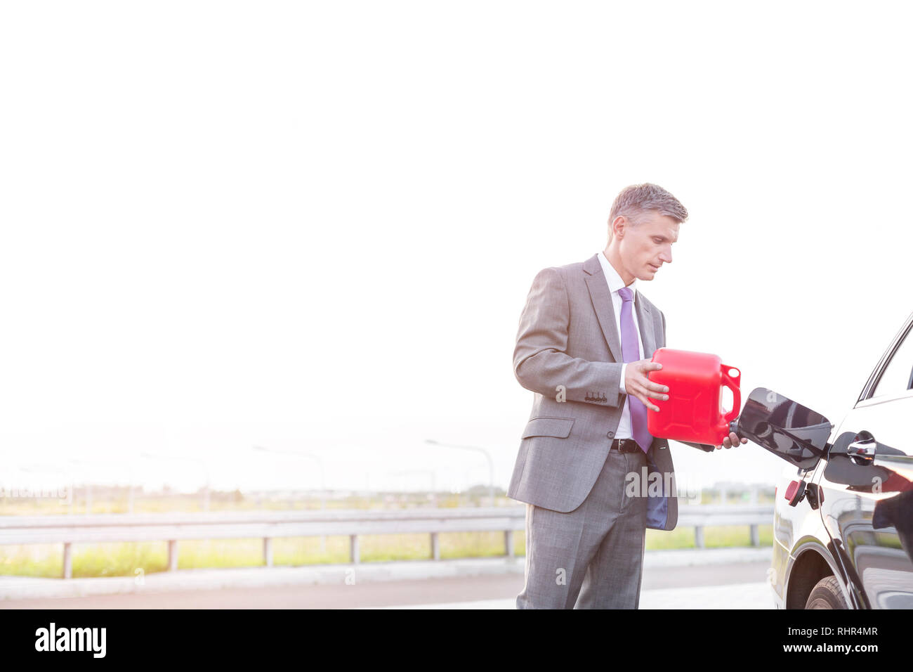 Mature executive fueling car with canister against sky Stock Photo