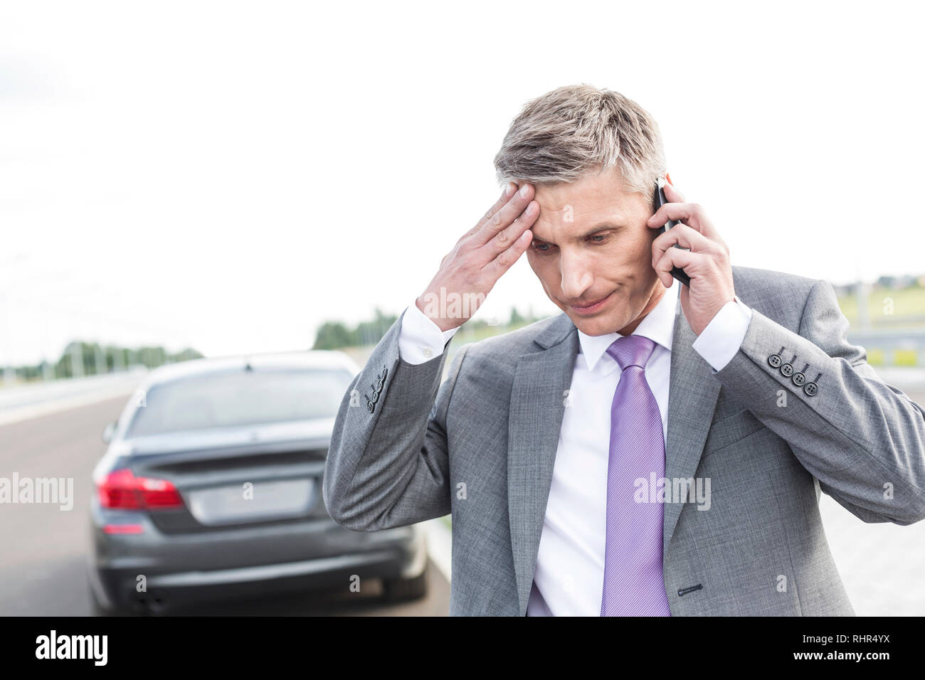 Tensed businessman talking on mobile phone against breakdown car Stock Photo