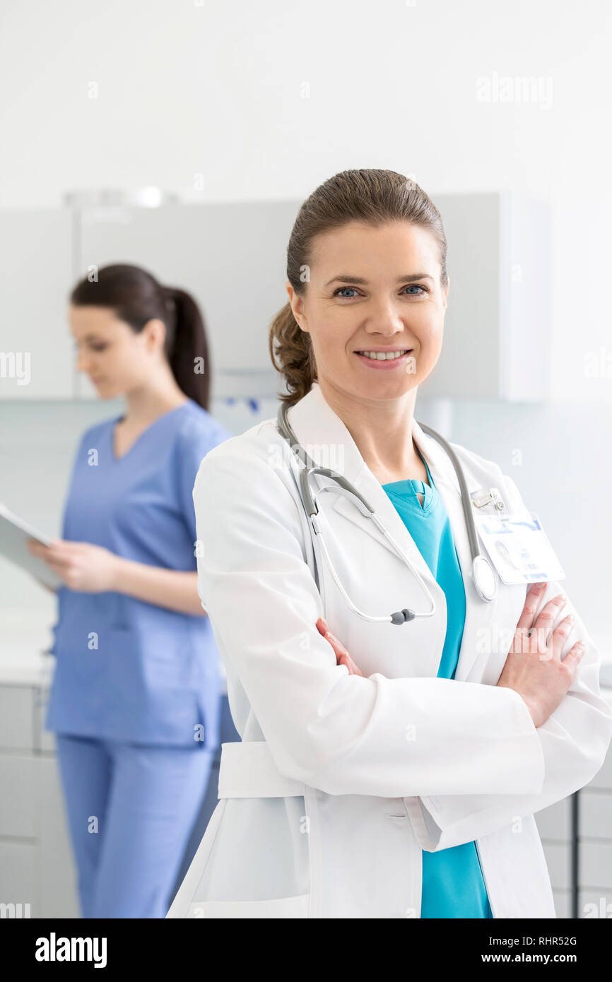 Portrait of smiling doctor with arms crossed standing against nurse in ...