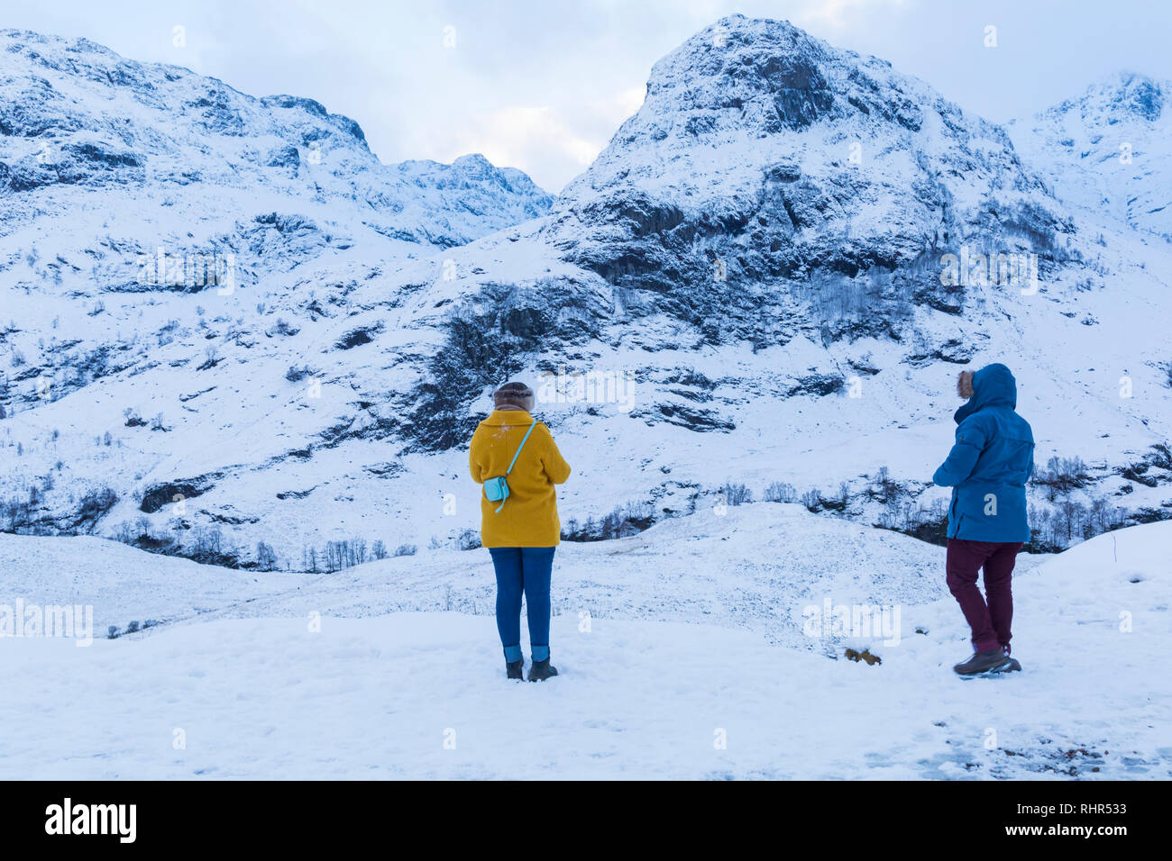 Tourists looking at the snow covered mountains of the Three Sisters  from the viewpoint off A82 at Glencoe, Highlands, Scotland in winter Stock Photo
