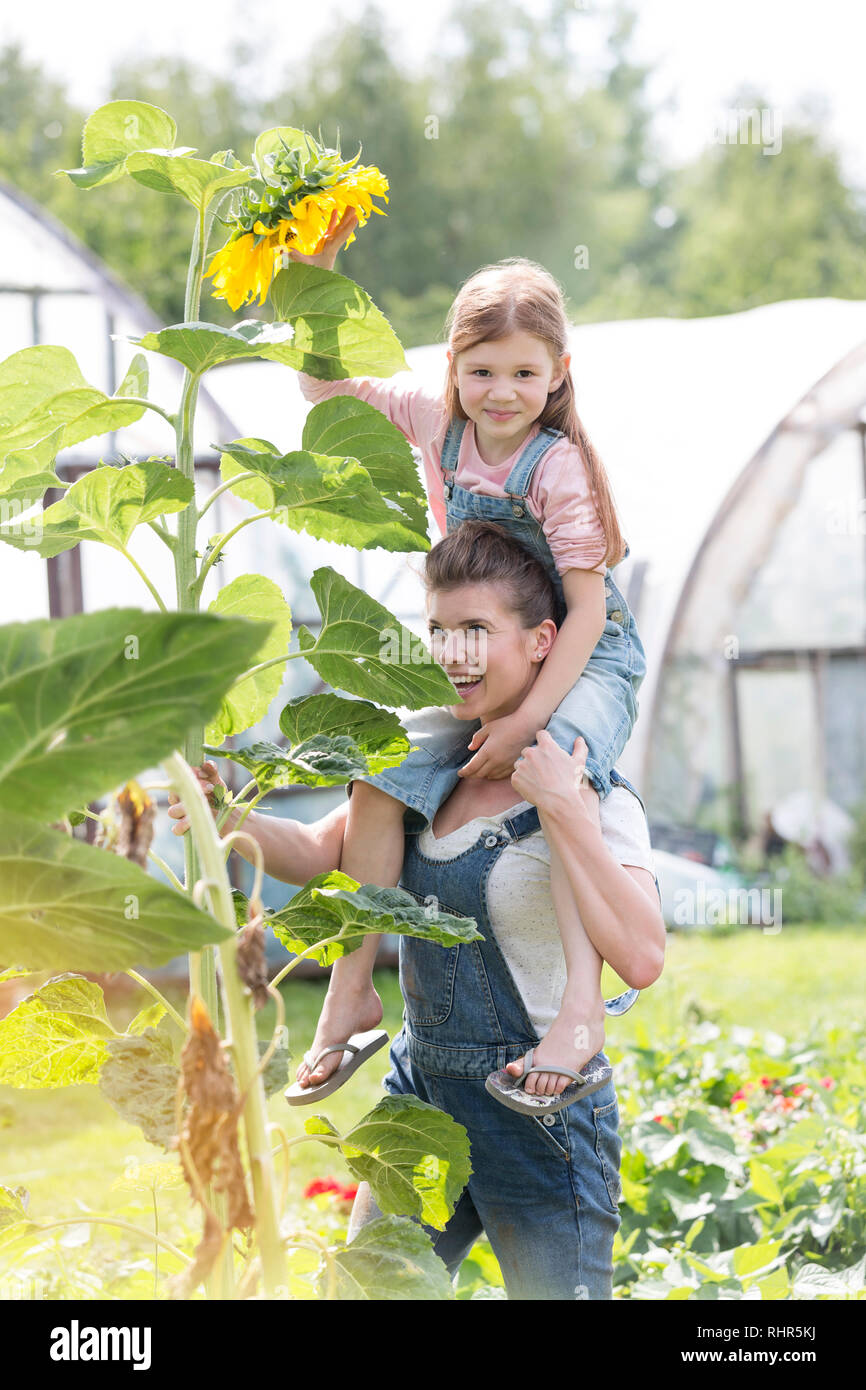 Smiling mother carrying daughter on shoulders by sunflower plant at farm Stock Photo