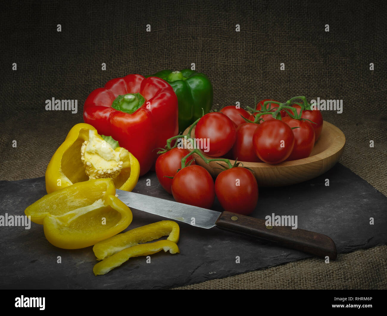 Sweet peppers and red tomatoes, still life. Light painting. With retro knife and slate rustic background. Stock Photo