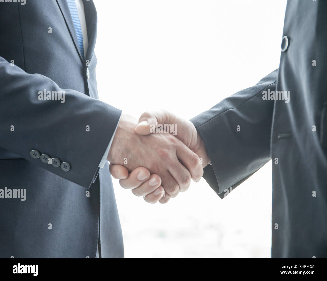 Two businessmen shaking hands standing by windows in office Stock Photo