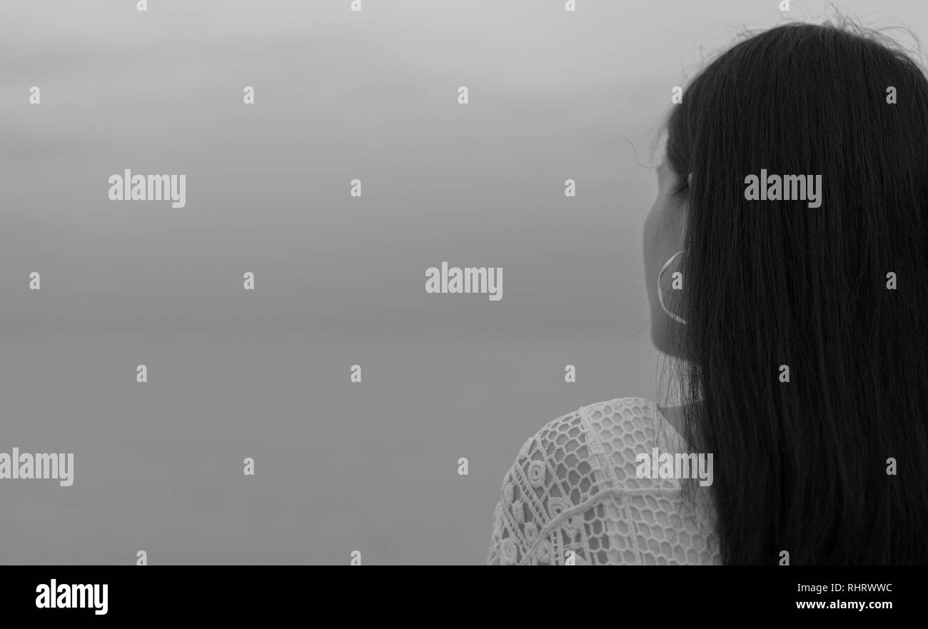 Pensive lonely young Asian woman. Back view of woman with sad feeling in black and white scene at the sea. Depressed and stressed girl stand Stock Photo
