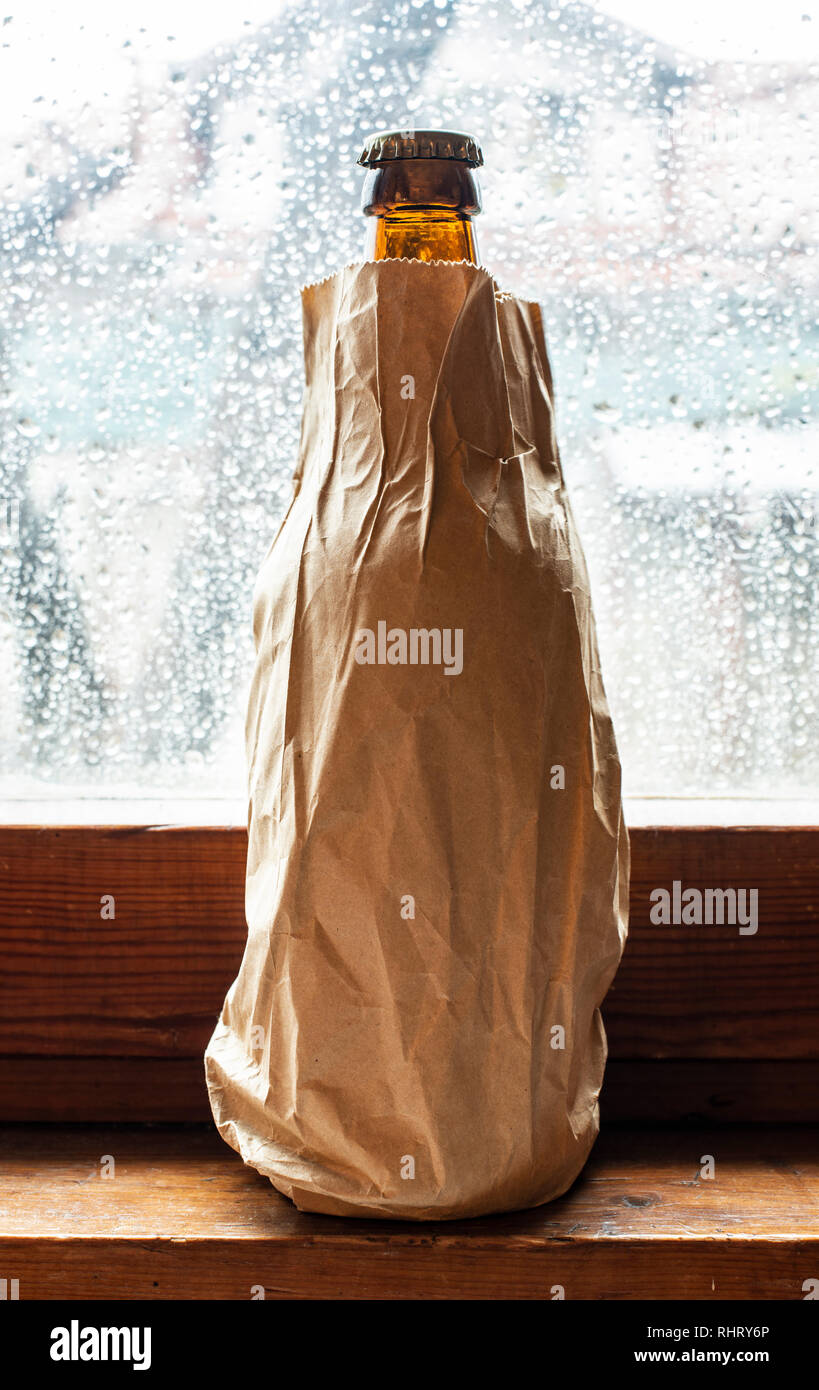 Bottle with alcohol in a brown pack paper placed to the window at rainy