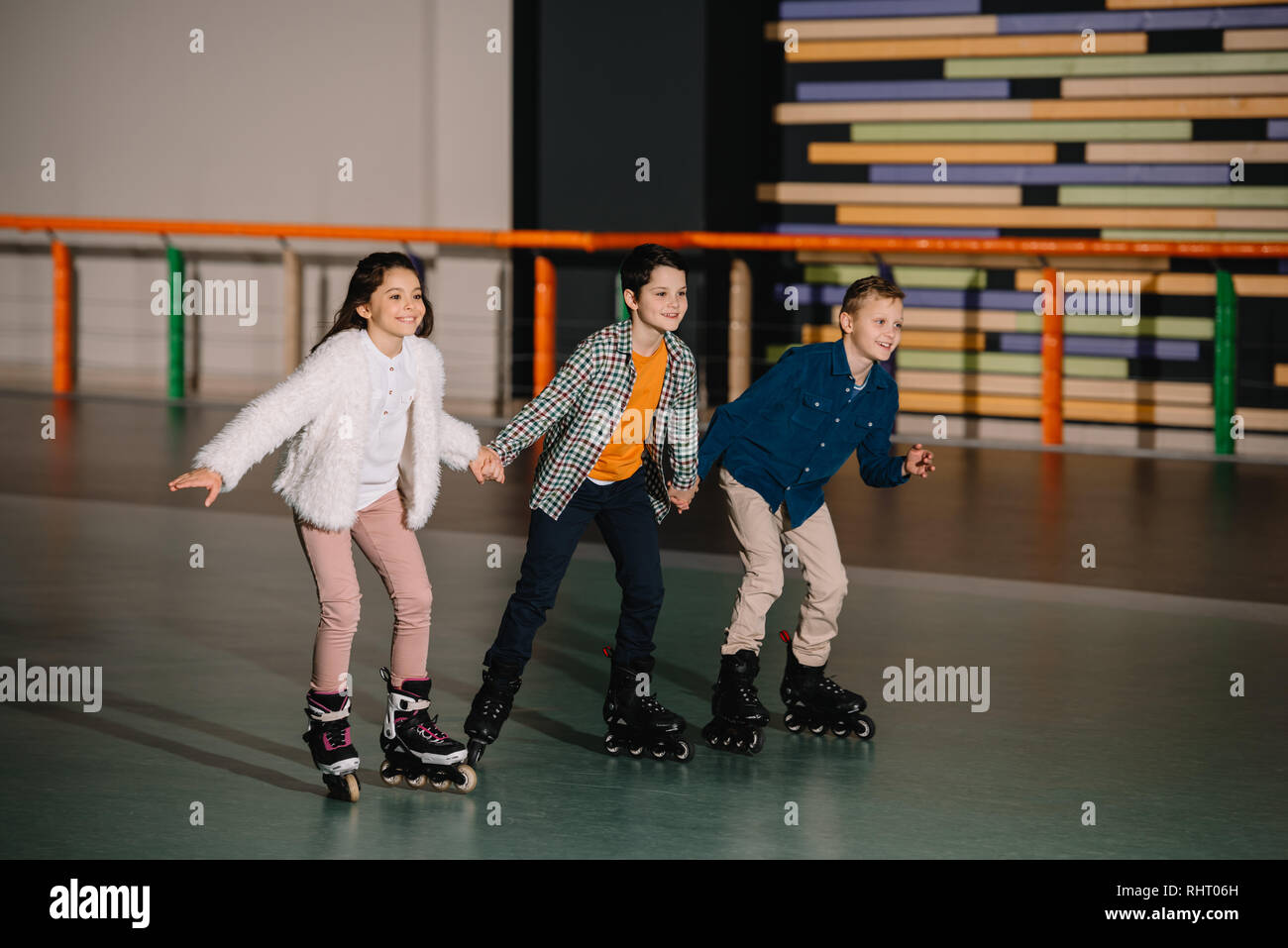 Three happy smiling children skating in roller rink with holding hands