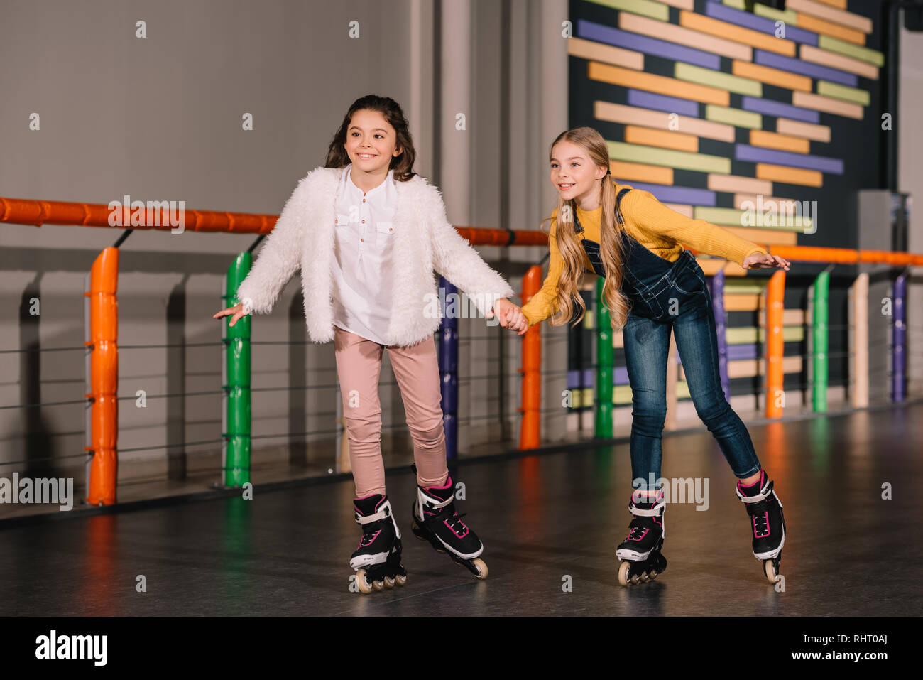 Cute sisters holding hands while skating on roller rink Stock Photo