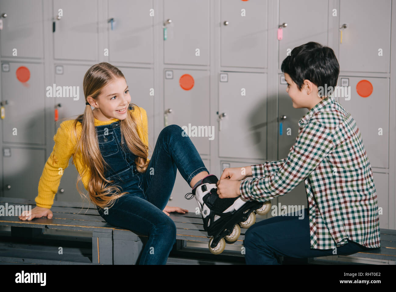 Kid in checkered shirt helps friend to putting on roller skates Stock Photo