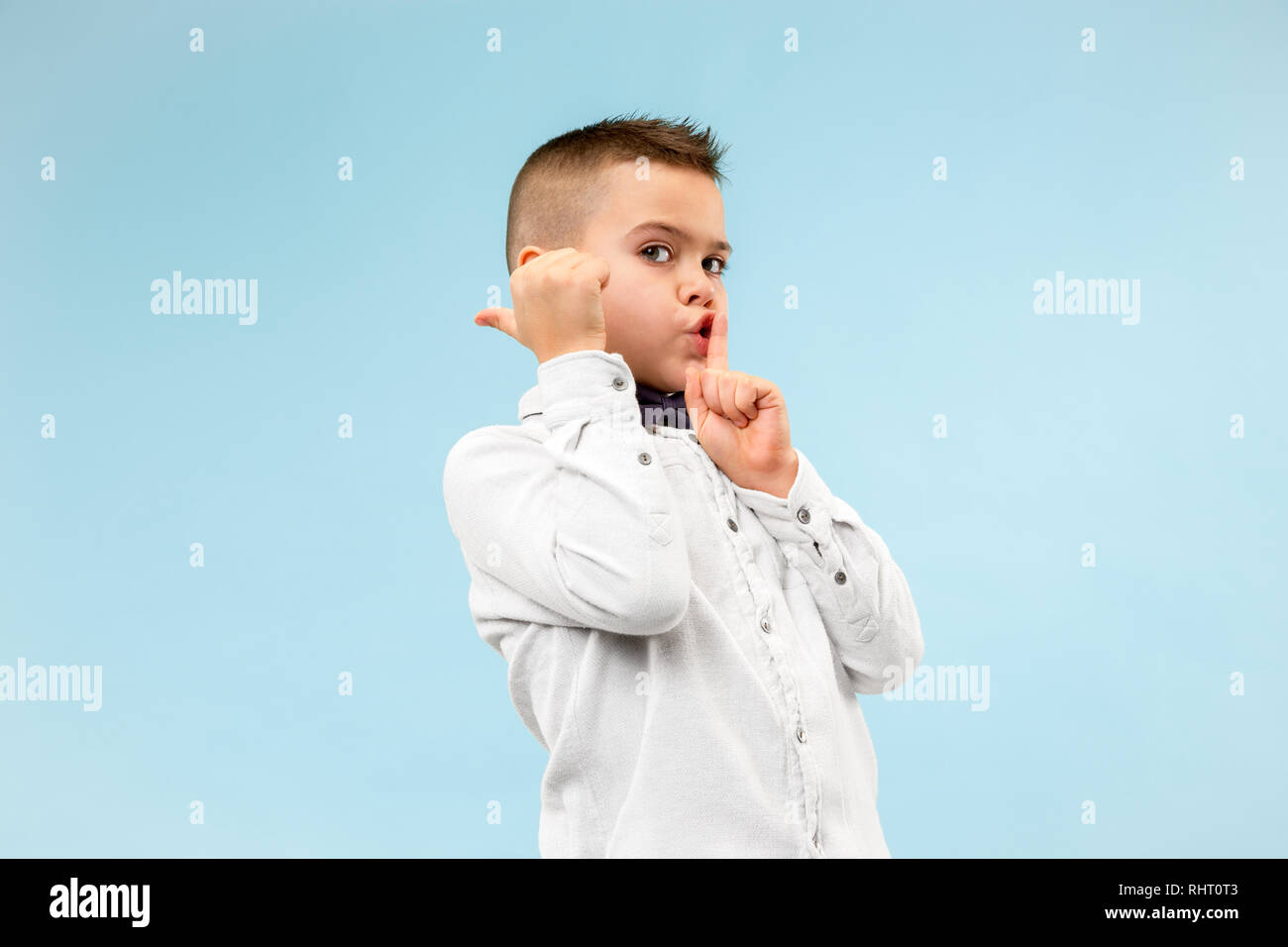 Secret, gossip concept. Teen boy whispering a secret behind his hand. Child isolated on trendy blue studio background. Human emotions, facial expression concept. Stock Photo