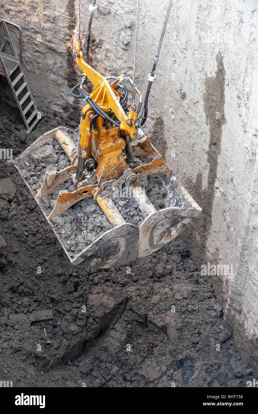 Construction site. A Dredge clamshell, rises a full bucket of muddy earth. Stock Photo