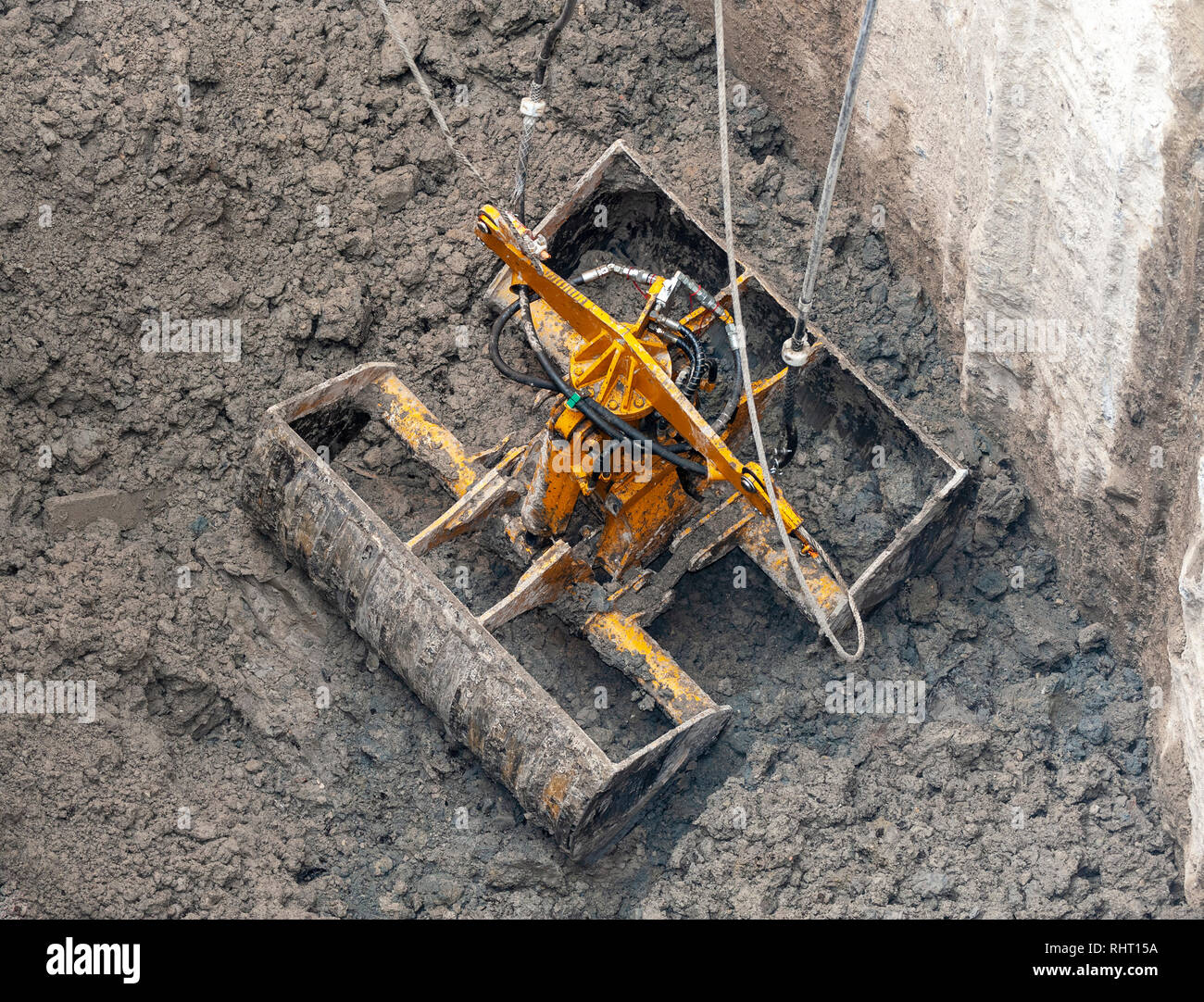 Construction site. A clamshell Dredge, placed in the mud, in an open position, is about to raise a full bucket of dirt. Stock Photo