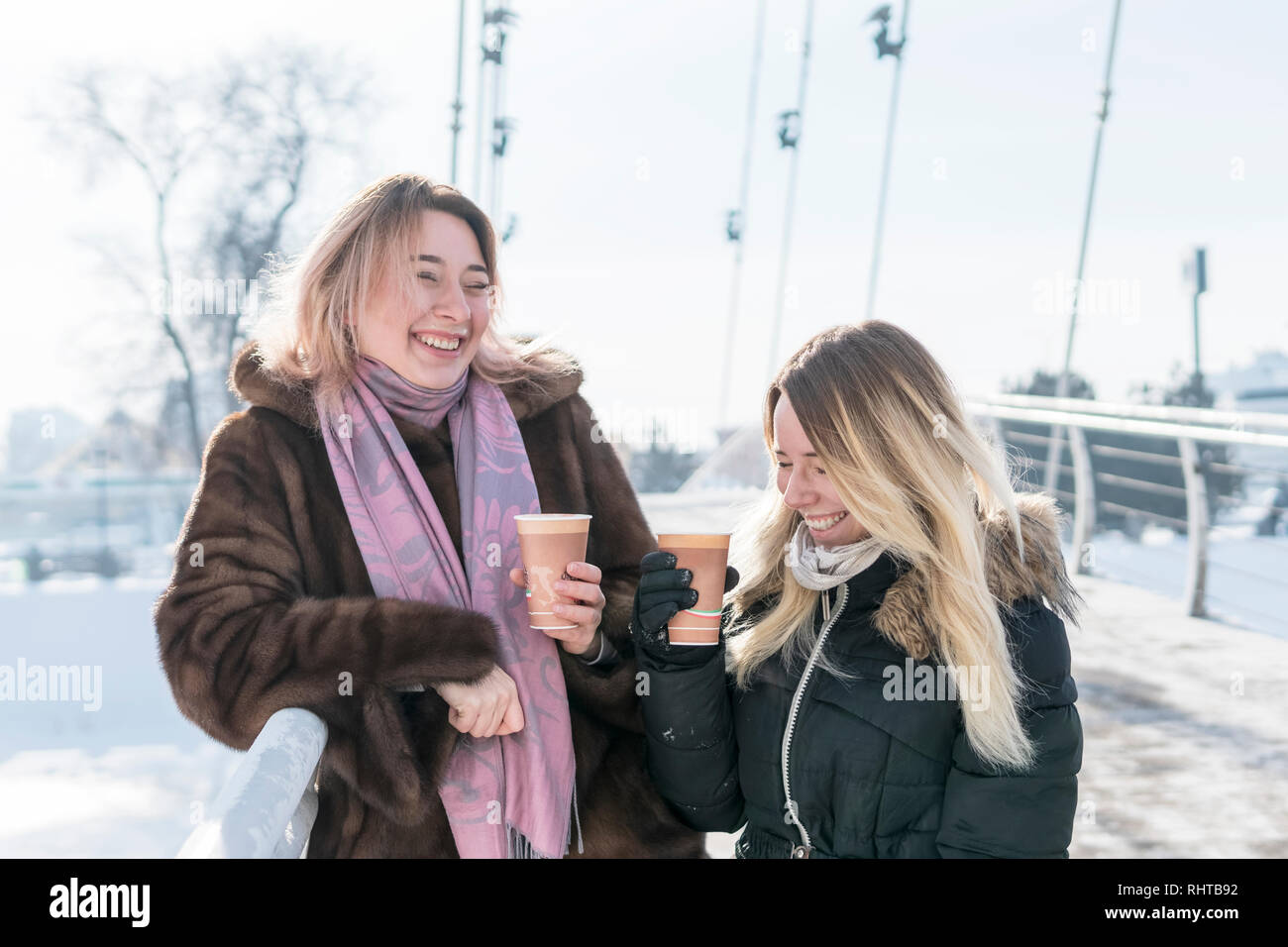 two women standing on the bridge laughing and drinking coffee with foam ...