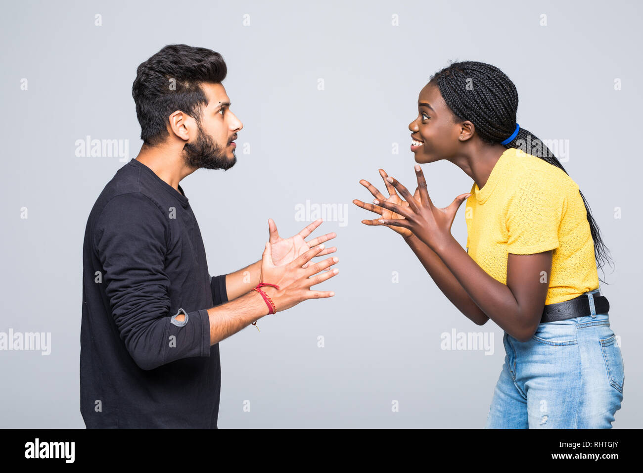 Excited surprised young interracial couple dressed in identical clothes and eyeglasses keeping clenched fists at their faces, screaming, opening mouth Stock Photo