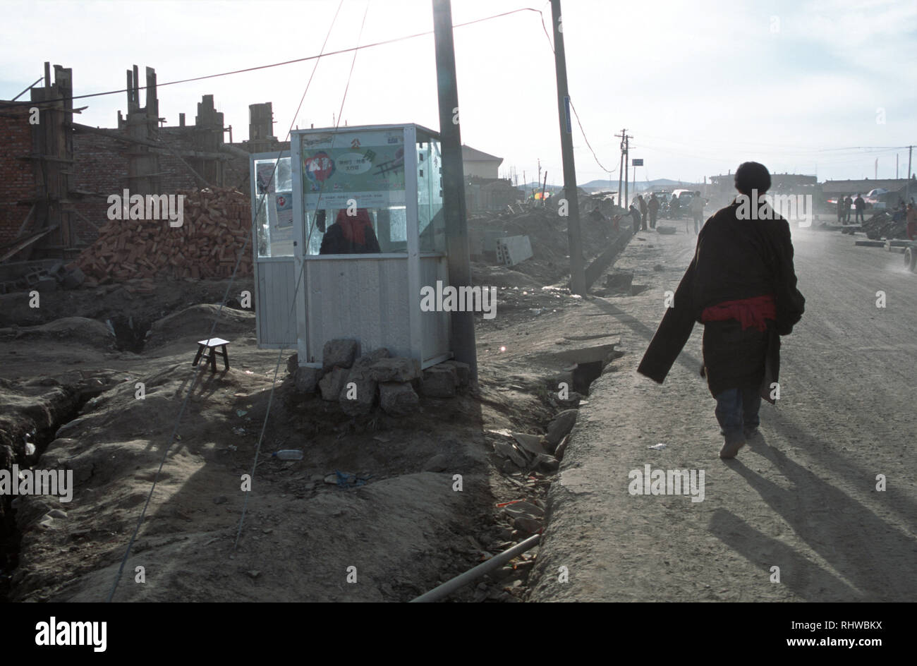 A Khampa man, characteristic wearing a traditional chuba cloak with one arm free and the other's sleeve hanging down to his knees, walks past the town Stock Photo