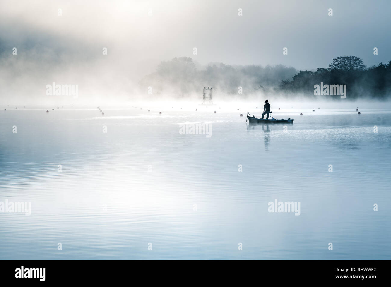 the silhouette of a fisher man with his boat on a misty moring at Lake ...