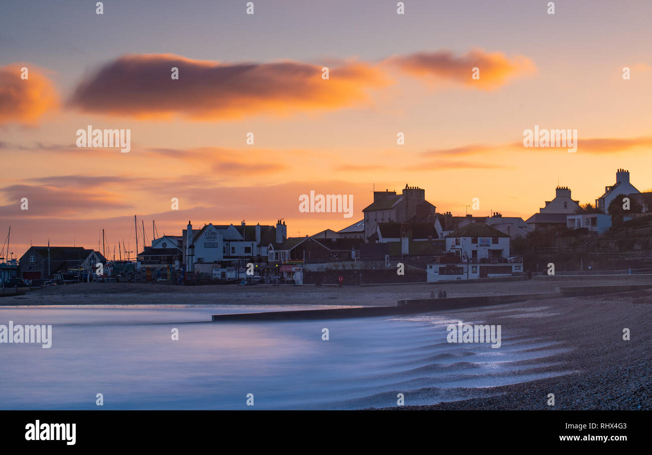 Lyme Regis, Dorset, UK. 4th February 2019. UK Weather: The sky glows orange as the sun sets over the seafront buildings and the Cobb at Lyme Regis after a day of rain and high winds. Credit: Celia McMahon/Alamy Live News Stock Photo